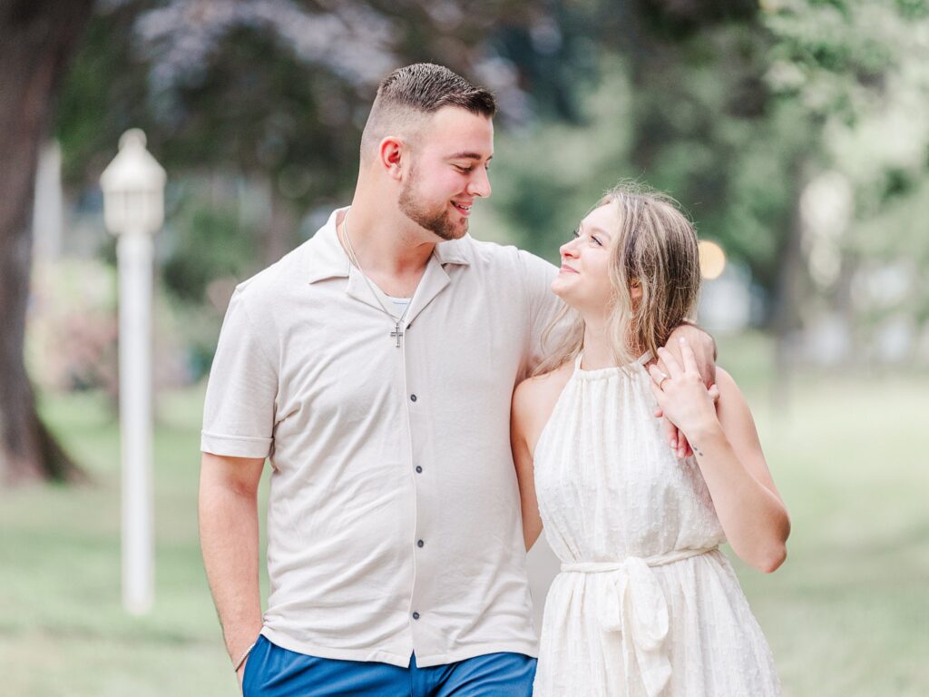 Engaged couple holding hands and smiling while walking barefoot along the shoreline during a beach engagement session